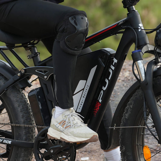 A person wearing knee pads and boots is riding a black electric bicycle with the "PUJH" brand logo.